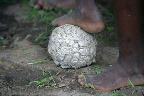 Ein Fuss eines dunkelhäutigen kindes liegt auf einem selbst gemachten fussball aus schnur und plastik