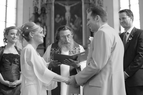 hochzeitsfotografie schwarz-weiss brautpaar vor dem altar und pfarrer, sich anschauend und hände haltend