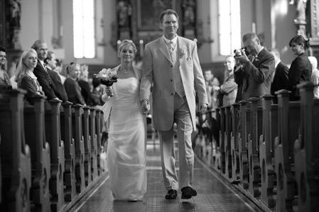 hochzeitsfotografie schwarz-weiss brautpaar läuft gemeinsam aus der kirche zwischen den zuschauern in den kirchenbänken