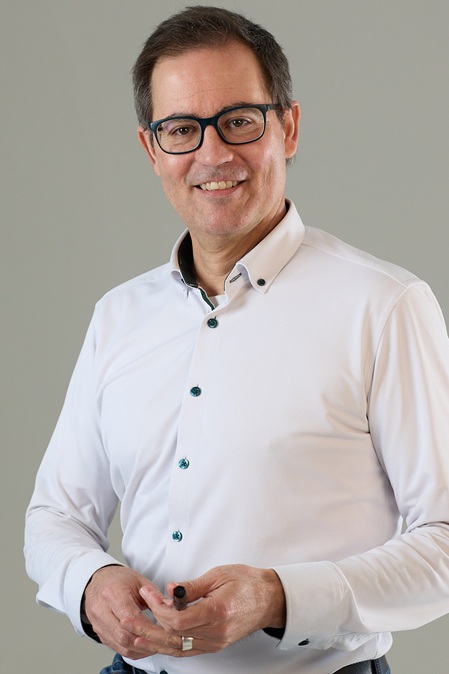 Herr um 50 Jahre mit weissem hemd und kurzem schwarzen haar mit brille und stift in hand businessportrait marc keller