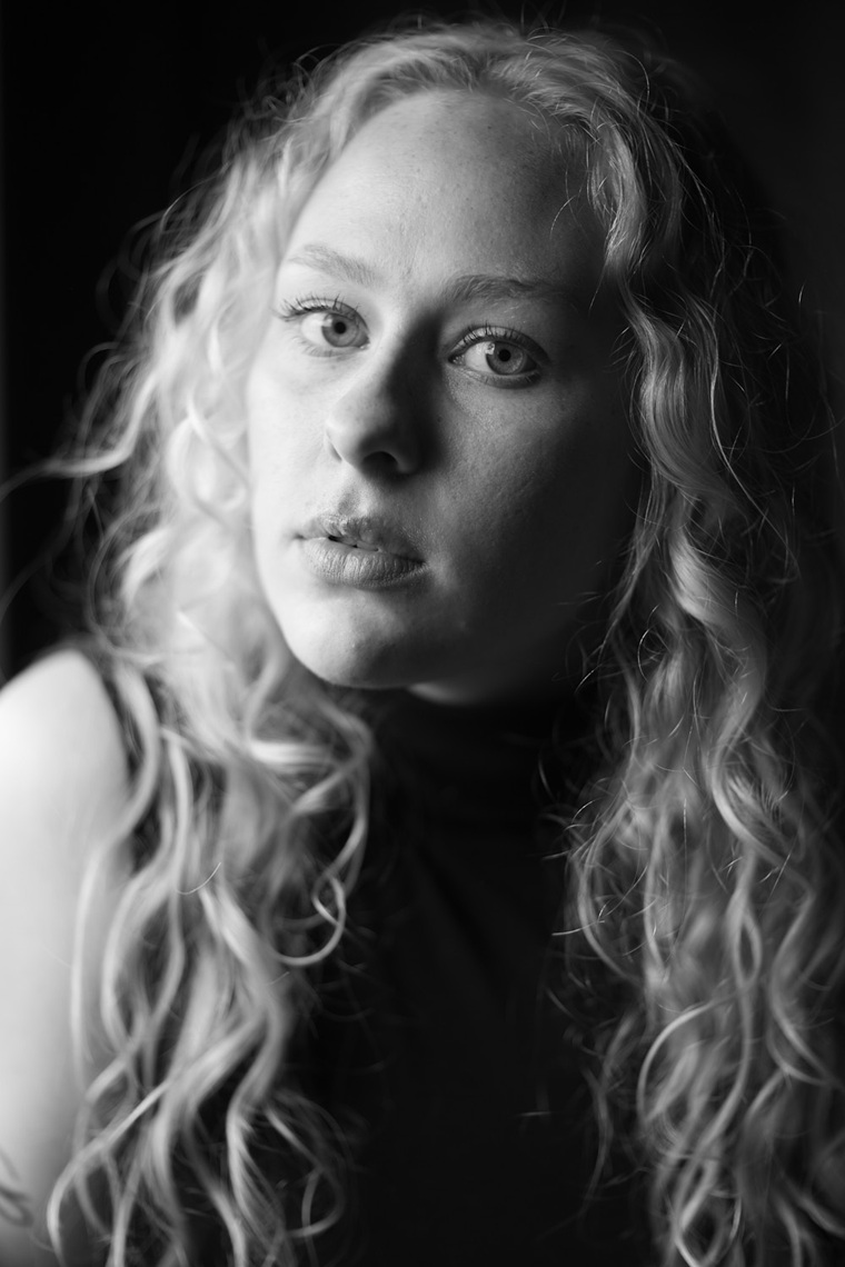 schwarz-weiss portrait einer jungen frau mit langen, gelockten blonden haaren, schwarzem ärmellosem top