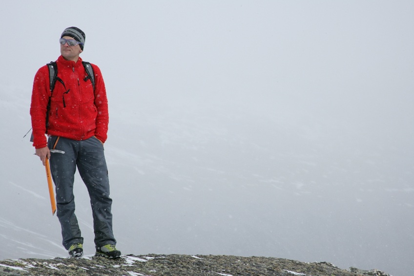Portrait von Emil Inauen, Outdoor-Sportler Bergsteiger mit roter Jacke und Eis-Pickel steht er und schaut in die Ferne Fotografie Marc Keller